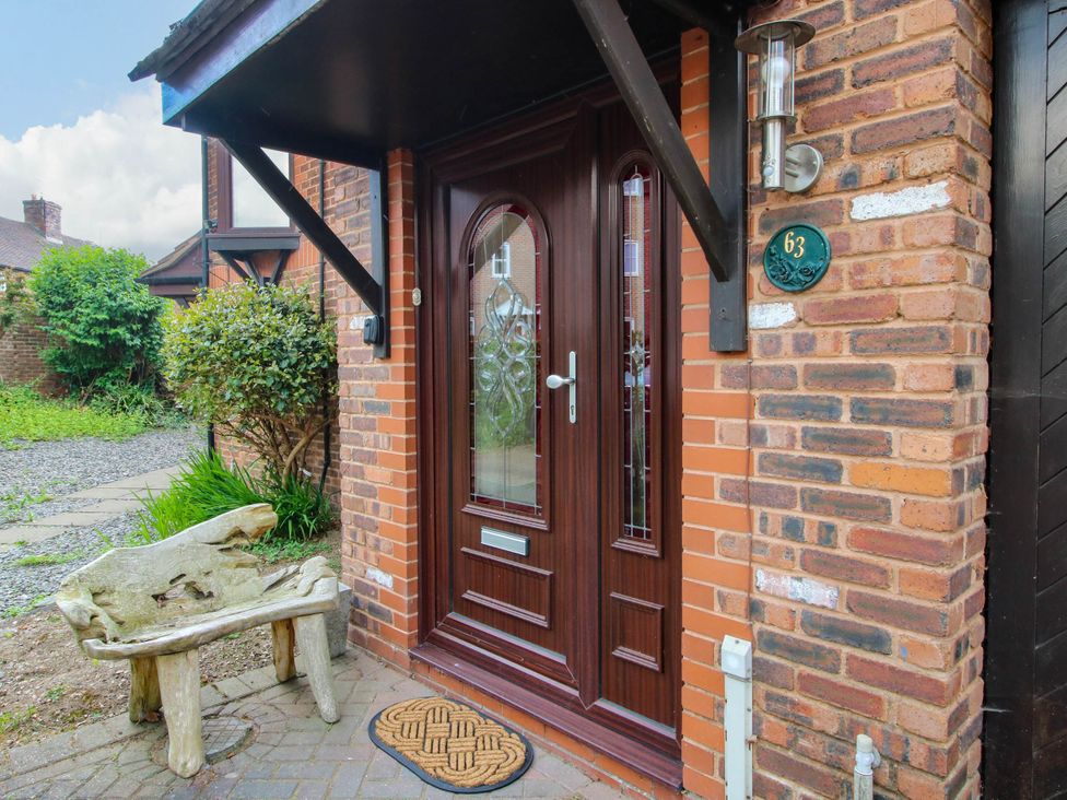 A wooden front door with glass panels under a black canopy with a decorative bench and a doormat at 63 Severn Street Bridgnorth