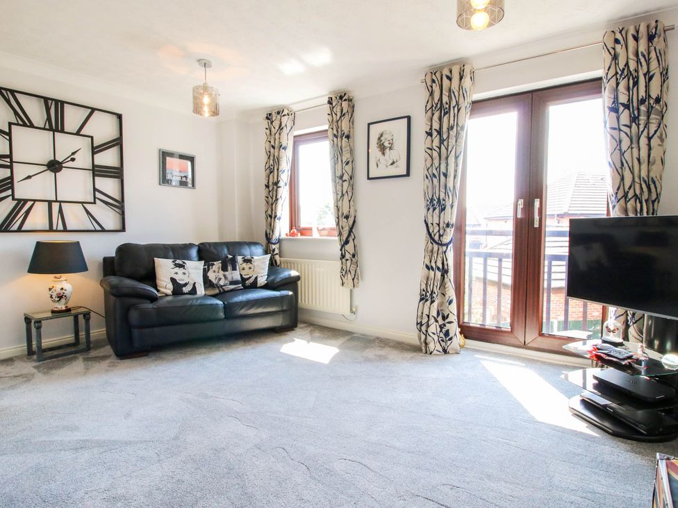 A living room with a black leather sofa cushions lamp clock tv and window curtains at 63 Severn Street Bridgnorth