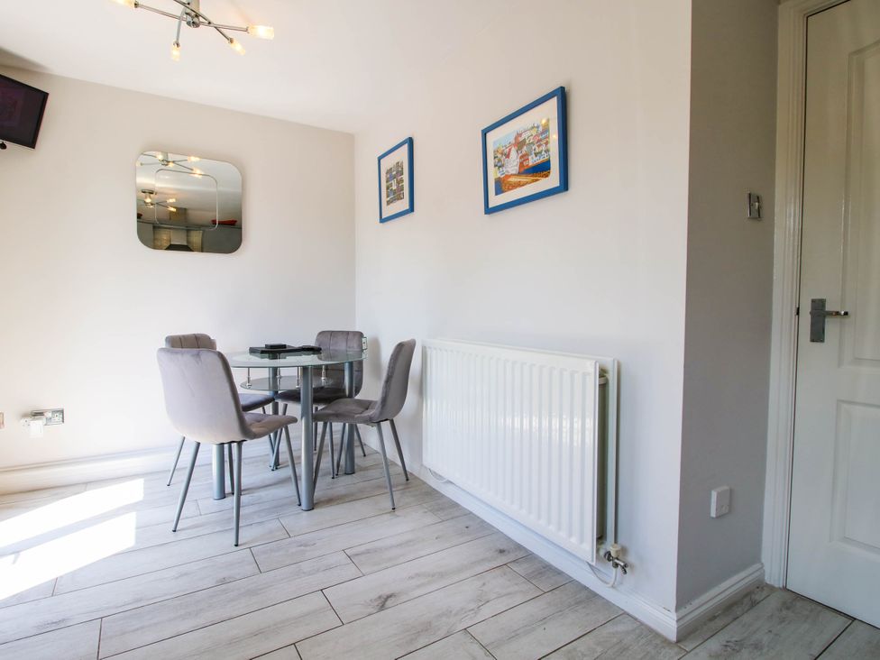 A dining area with a glass table and four grey chairs a white radiator two framed pictures on the wall and a white door at 63 Severn Street Bridgnorth