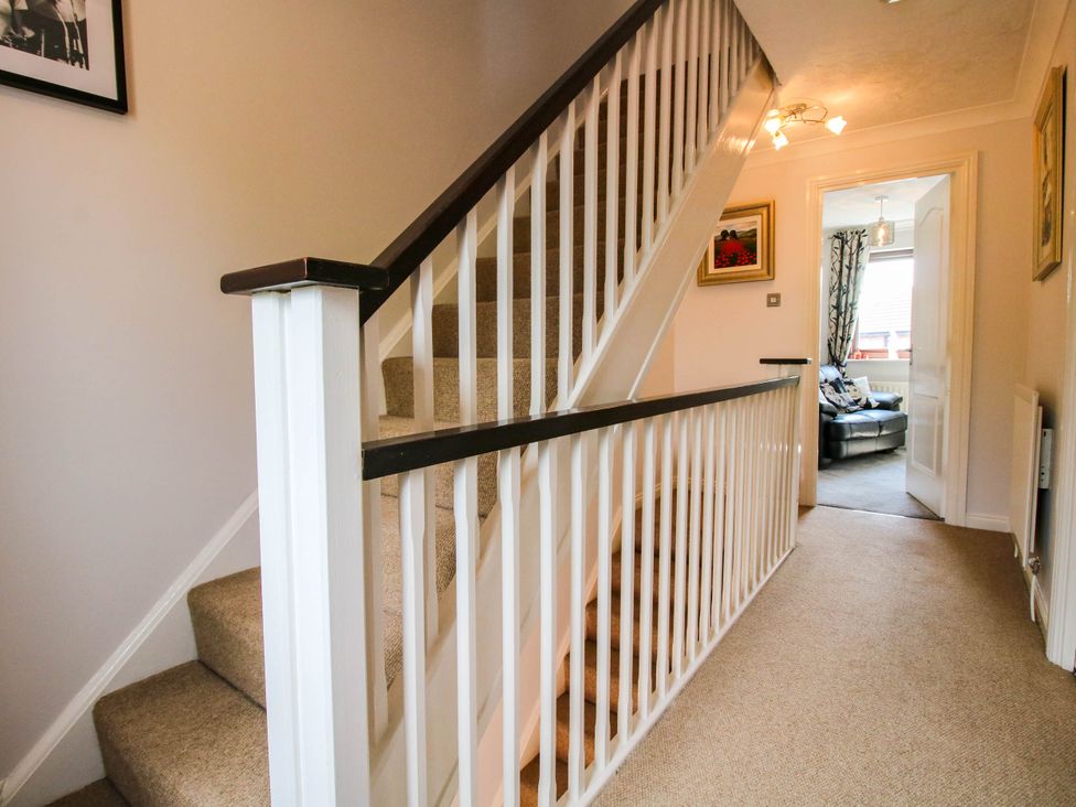 A hallway with carpeted stairs and white wooden banisters leading to a room with a black leather sofa at 63 Severn Street in Bridgnorth