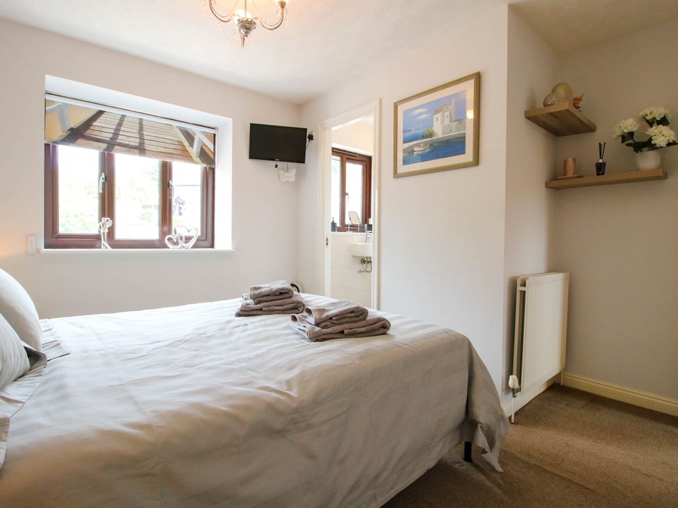 A bedroom with a bed and towels on it a window with a printed blind a small wall-mounted TV and a bathroom visible through an open door at 63 Severn Street in Bridgnorth