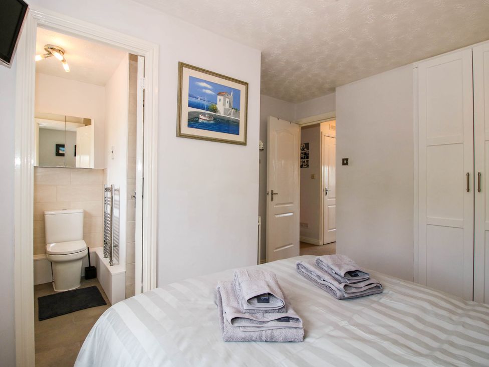 A bedroom with folded towels on the bed a doorway leading to a bathroom with a toilet and a hallway with an open door at 63 Severn Street in Bridgnorth