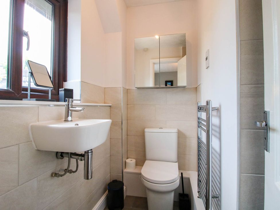 A bathroom with a wall-mounted sink a toilet a mirrored cabinet a window and a towel radiator at 63 Severn Street Bridgnorth