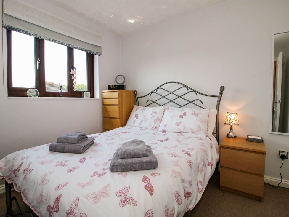 A bedroom with a metal bed frame with butterfly patterned bedding two wooden bedside tables with a lamp and drawers and a window with blinds at 63 Severn Street in Bridgnorth