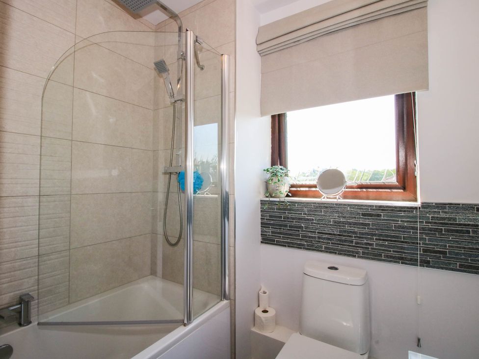 A bathroom with a bathtub and shower, toilet, window with blind, and a small plant at 63 Severn Street Bridgnorth