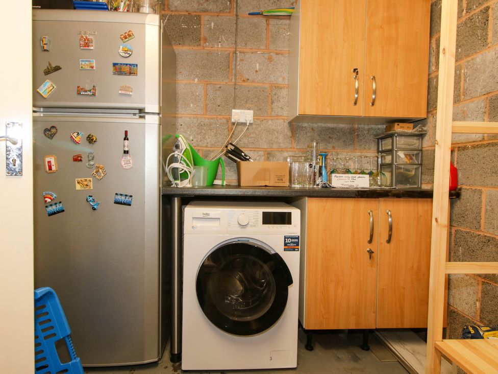 A utility room with a fridge covered in magnets a washing machine wooden cabinets and various kitchen items on the counter at 63 Severn Street Bridgnorth