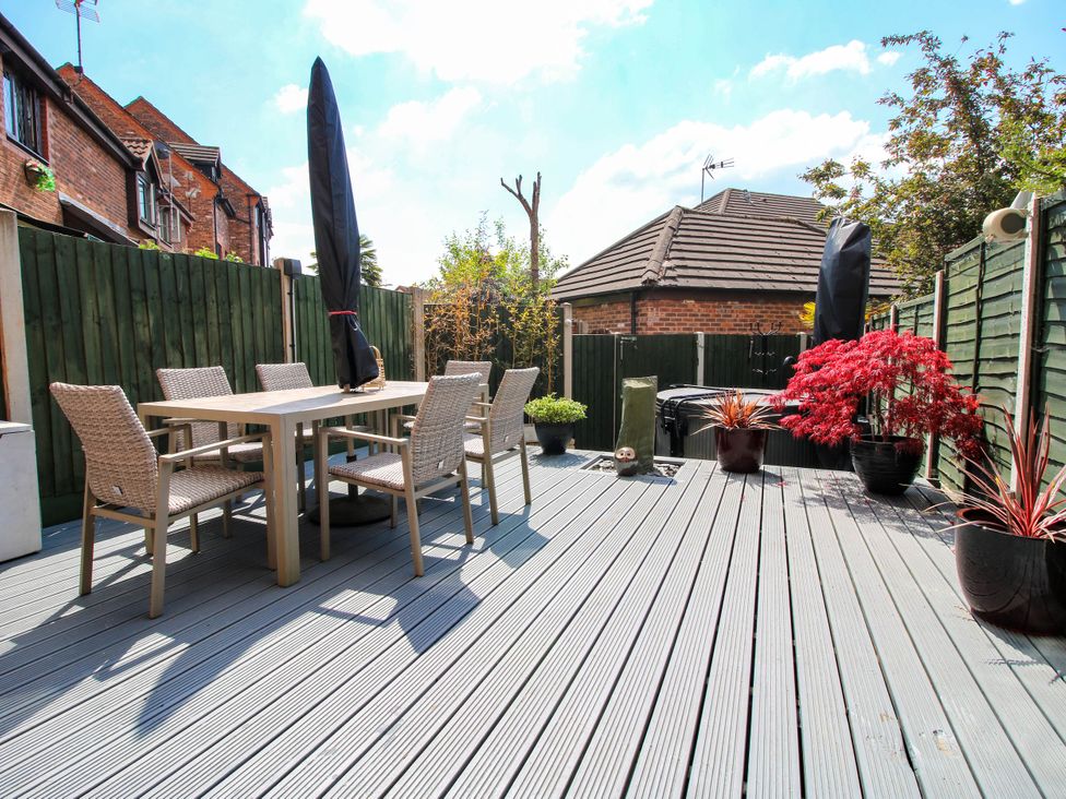 An outdoor decking area with a dining table and six chairs surrounded by green fences and potted plants at 63 Severn Street in Bridgnorth