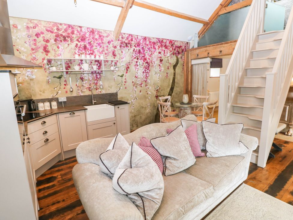 A living room with a sofa, kitchen unit and staircase at The Apple Store at Gileston Manor, Gileston near St Athan
