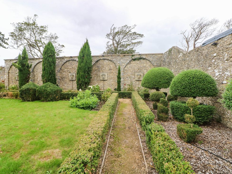 A garden with trimmed hedges and a stone wall at The Apple Store at Gileston Manor near St Athan