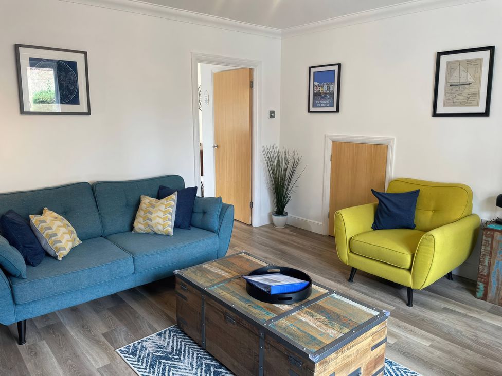 A living room with a blue sofa and yellow armchair at Plain Sailing in Weymouth