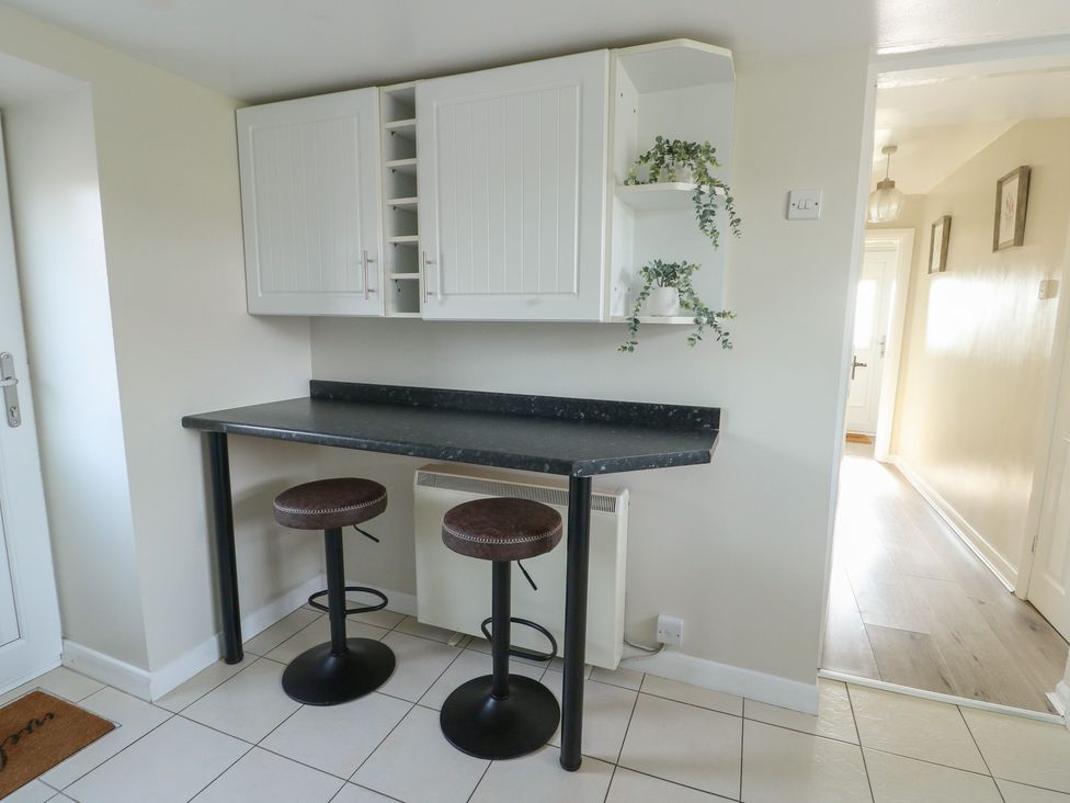 A kitchen with a countertop, bar stools and wall cabinet at Pentre Iago in Rhoscolyn