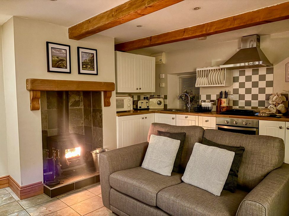 A living room with a fireplace and kitchen area at School House Cottage Newtown near Longnor