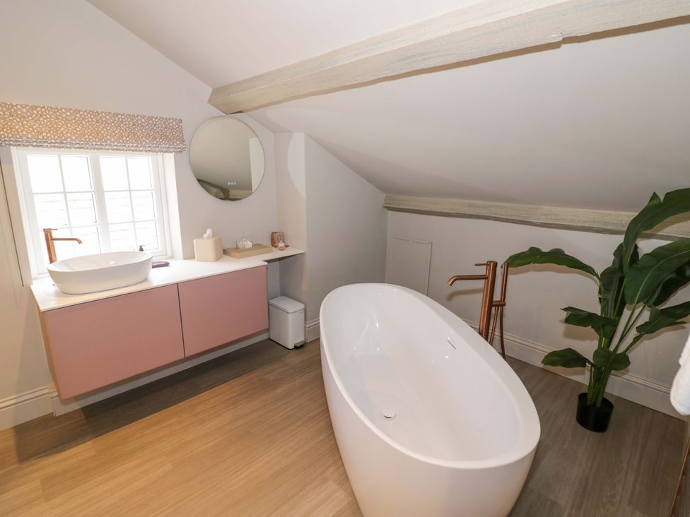A bathroom with a bathtub, sink, and mirror at Bay House Cottage in Broadway