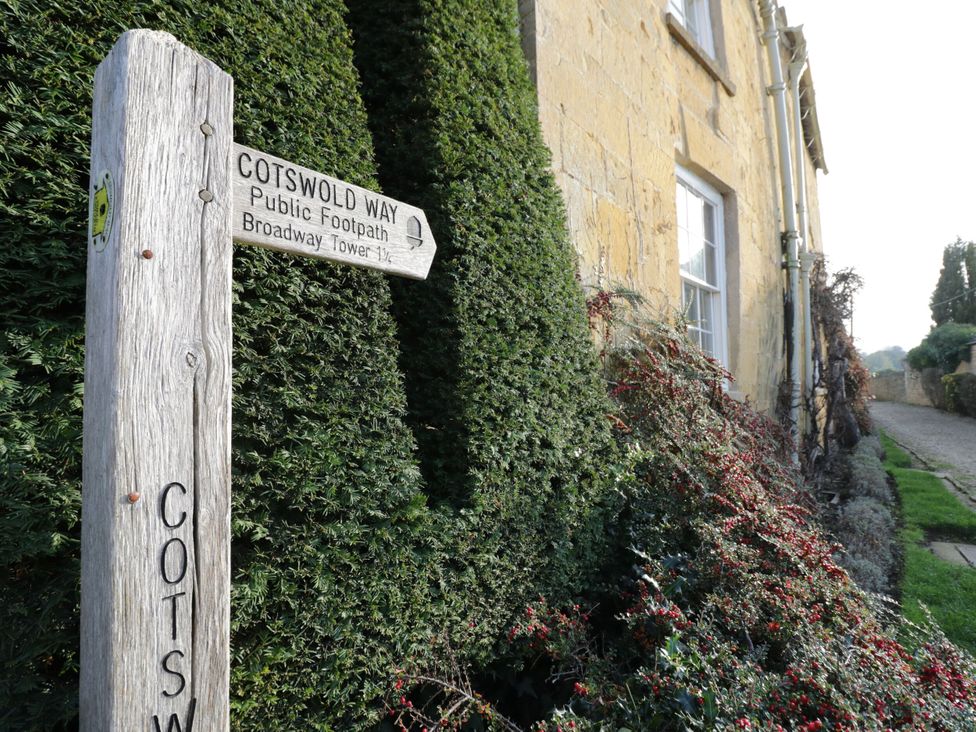 A signpost by a hedge and house at Bay House Cottage in Broadway