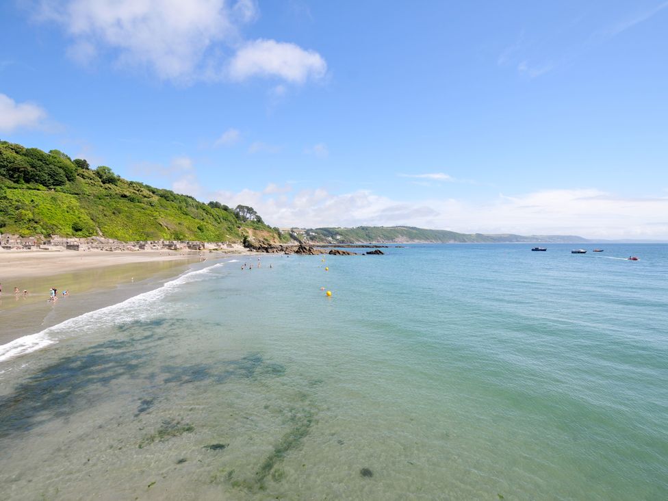 A beach scene with people swimming and boats in the water at Sea Pinks in Looe