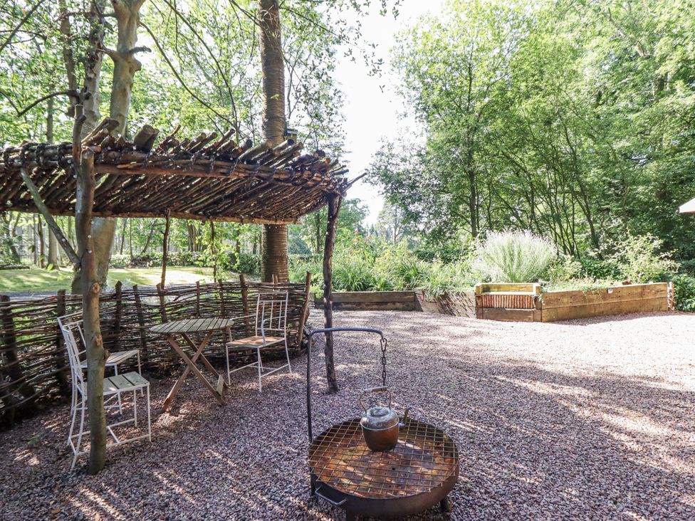 A garden with a table and chairs under a wooden shelter at Tanglewood Shepherds Hut in Welshpool