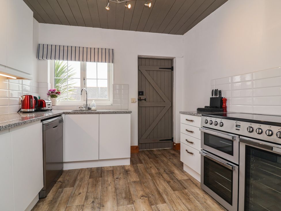 A kitchen with white cabinets, grey door, and stainless steel appliances at Cobblestone Cottage in Bude