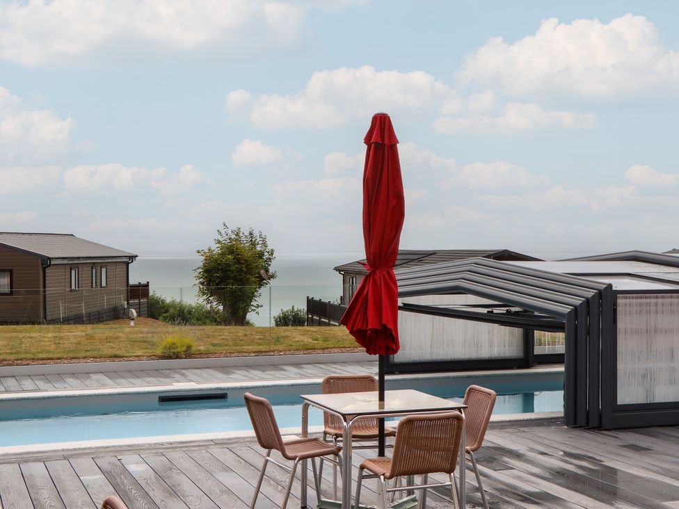 An outdoor area with a table and chairs by a swimming pool at Lodge 69 at Riviera Bay Coastal Retreat in Brixham
