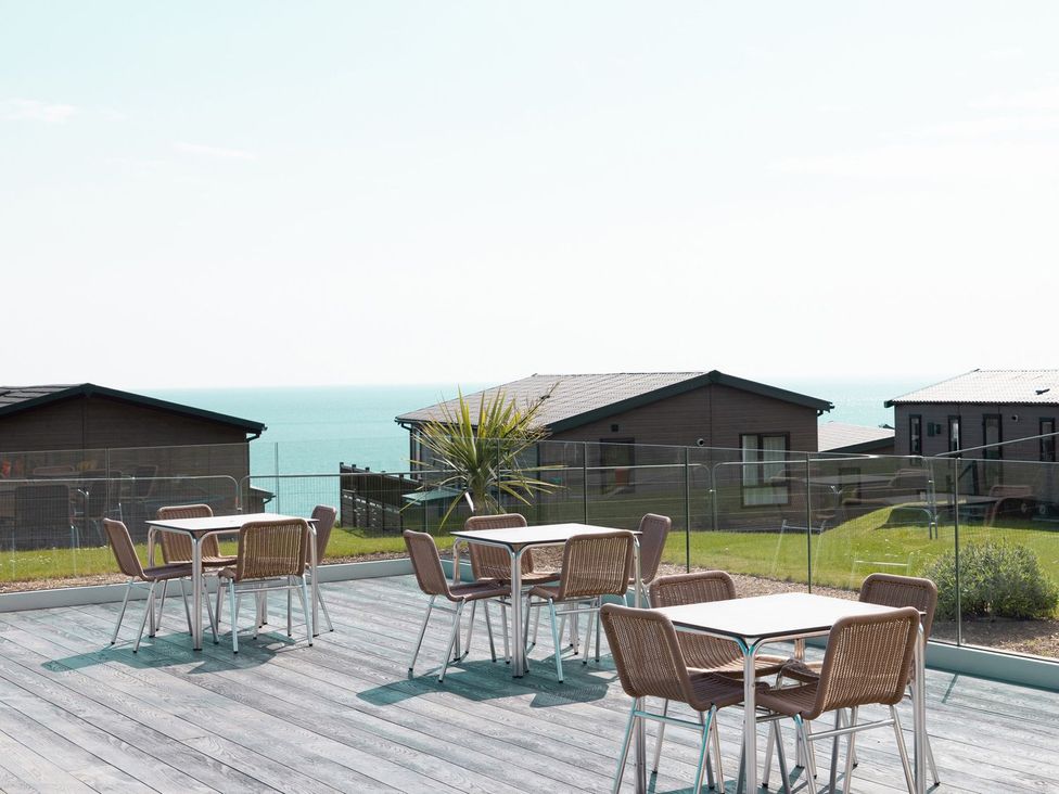 An outdoor seating area with tables and chairs overlooking the sea at Lodge 11 at Landscove Holiday Park in Brixham