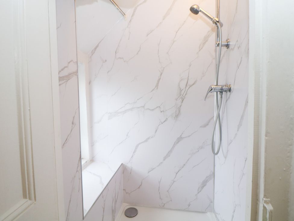 A shower with marble walls and a showerhead at Roseville in Cromford