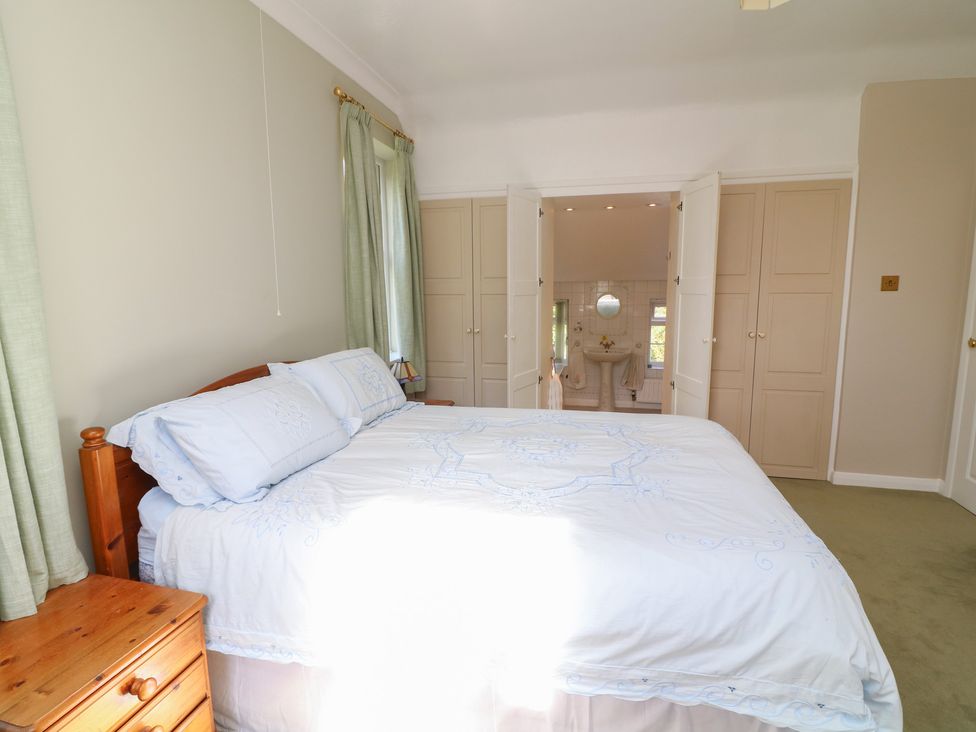 A bedroom with a bed and nightstand leading to a bathroom at Larkspur Cottage in Alford
