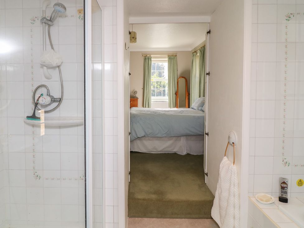 A bedroom with a bed and a shower visible at Larkspur Cottage in Alford