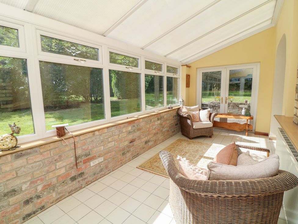 A conservatory with seating and large windows at Larkspur Cottage in Alford
