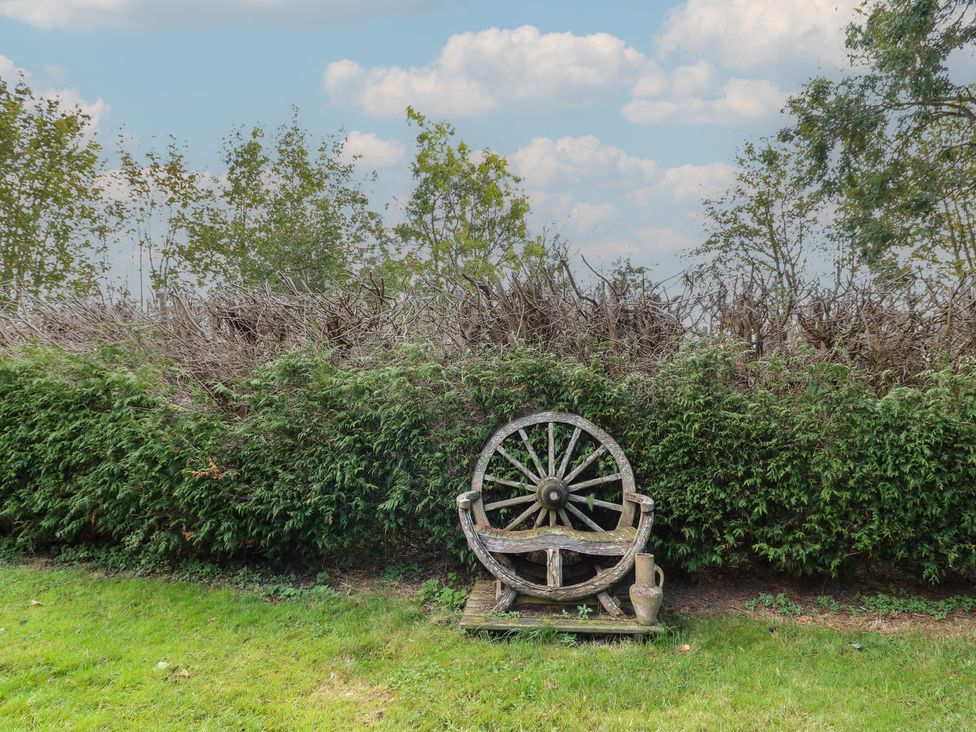 A wooden wheel and seat in a garden at Larkspur Cottage in Alford