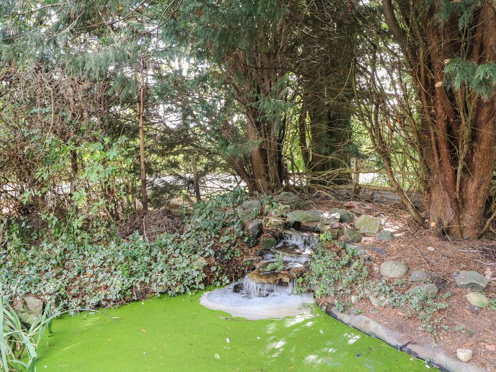 A pond with a small waterfall surrounded by greenery at Larkspur Cottage in Alford