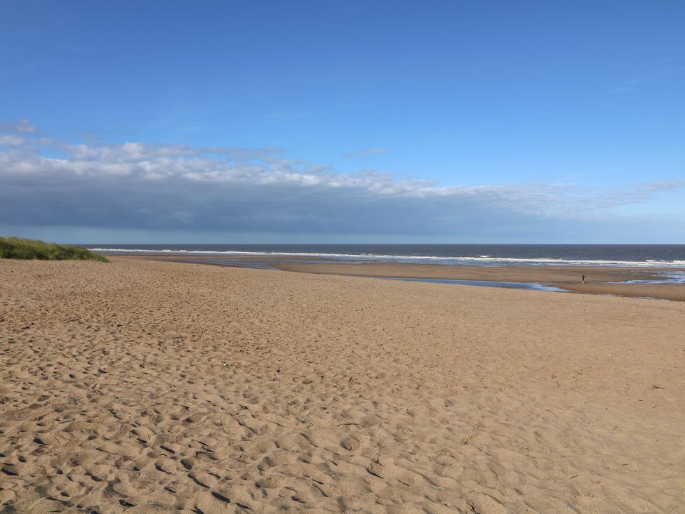 A beach with sand and ocean under a blue sky at Larkspur Cottage in Alford