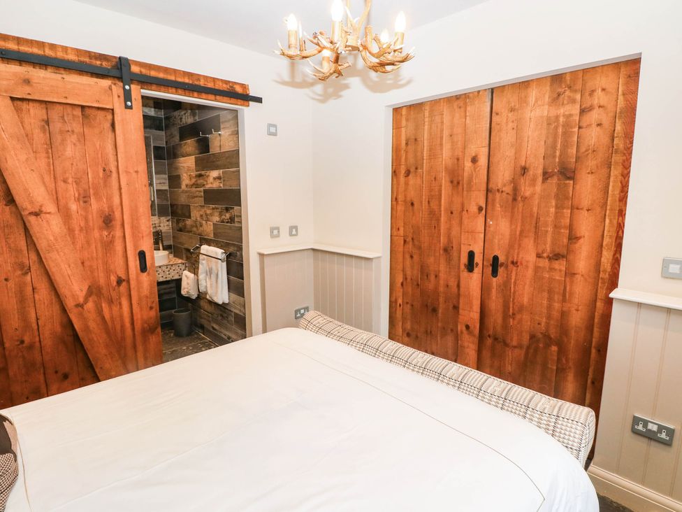 A bedroom with a bed and sliding door leading to a bathroom at The Stalls at Gileston Manor St Athan