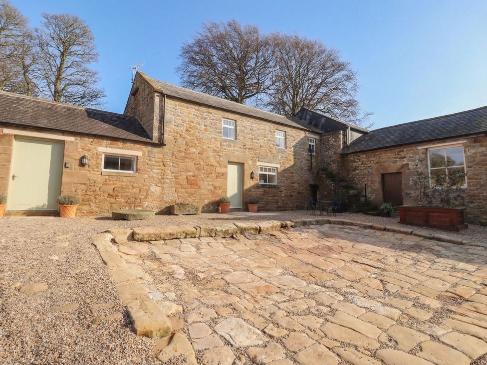 An outdoor area with buildings and stone path at Cragg Lodge in West Woodburn