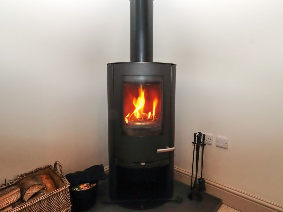 A wood stove with flames and a basket of logs at Cragg Lodge West Woodburn