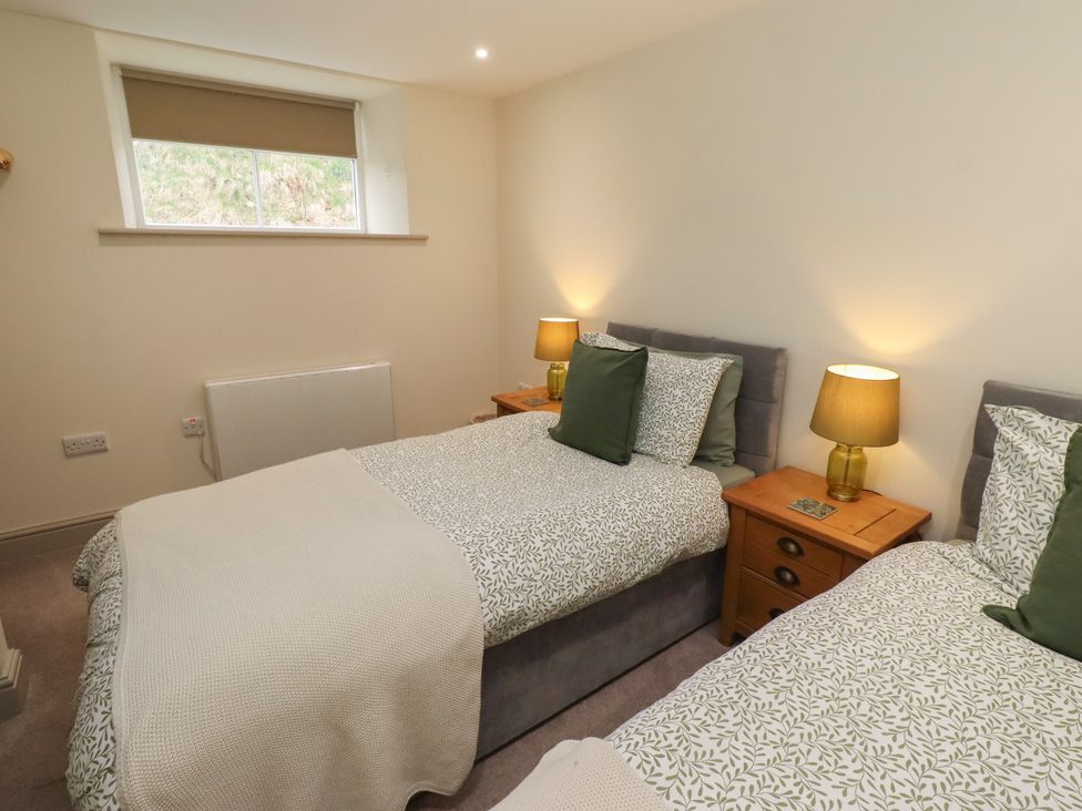 A bedroom with two beds and lamps on bedside tables at Cragg Lodge in West Woodburn