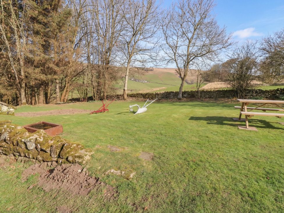 A garden with grass, wheelbarrow and trees at Cragg Lodge West Woodburn