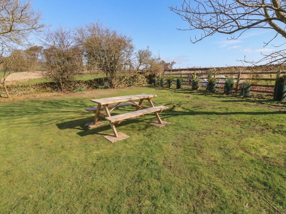 A picnic table on grass with trees and a fence at Cragg Lodge, West Woodburn