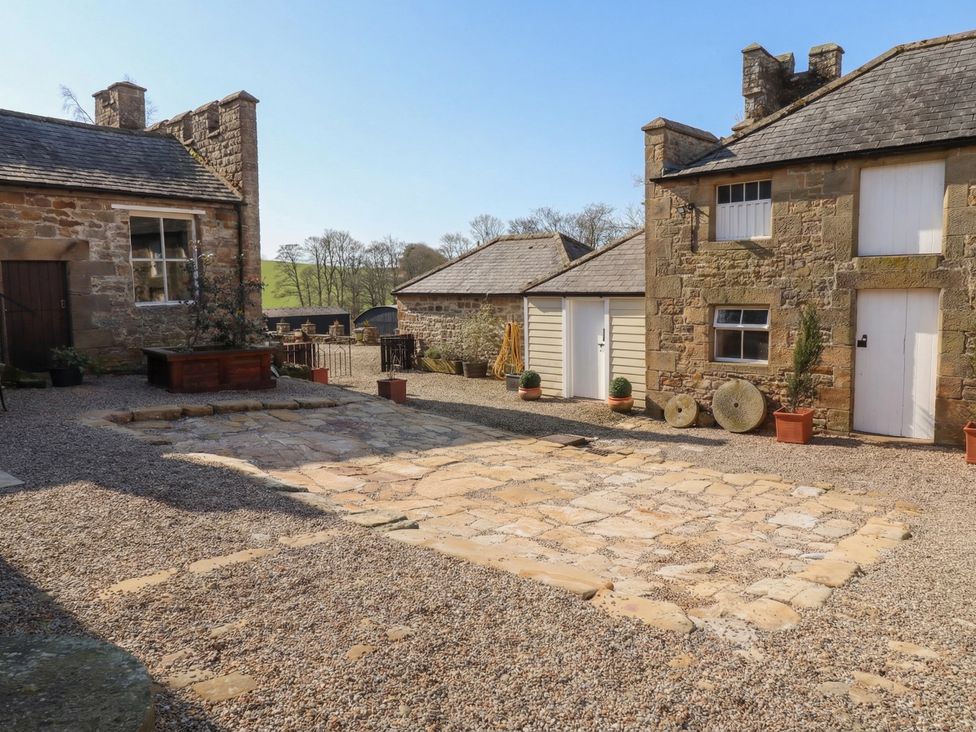 An outdoor area with stone patio and buildings at Cragg Lodge, West Woodburn