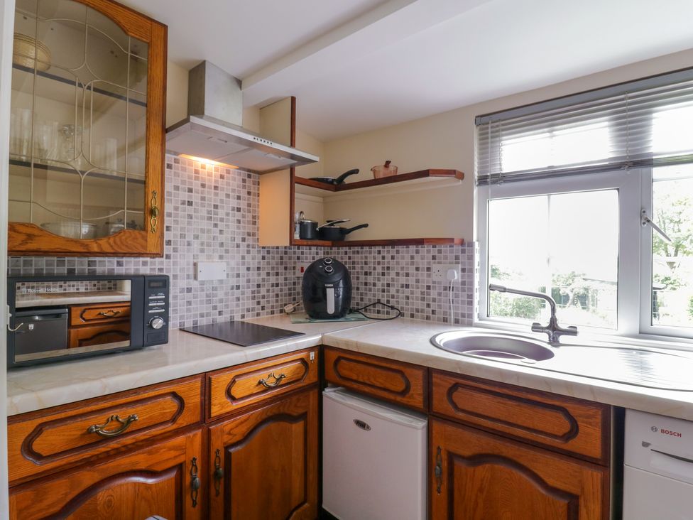 A kitchen with wooden cabinets a microwave an air fryer a stovetop a sink under a window and tiled backsplash at The Cottage in Sudbury
