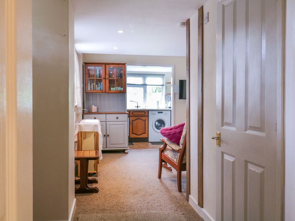 A hallway leading to a kitchen with a washing machine and wooden cabinets and a wooden chair with cushions