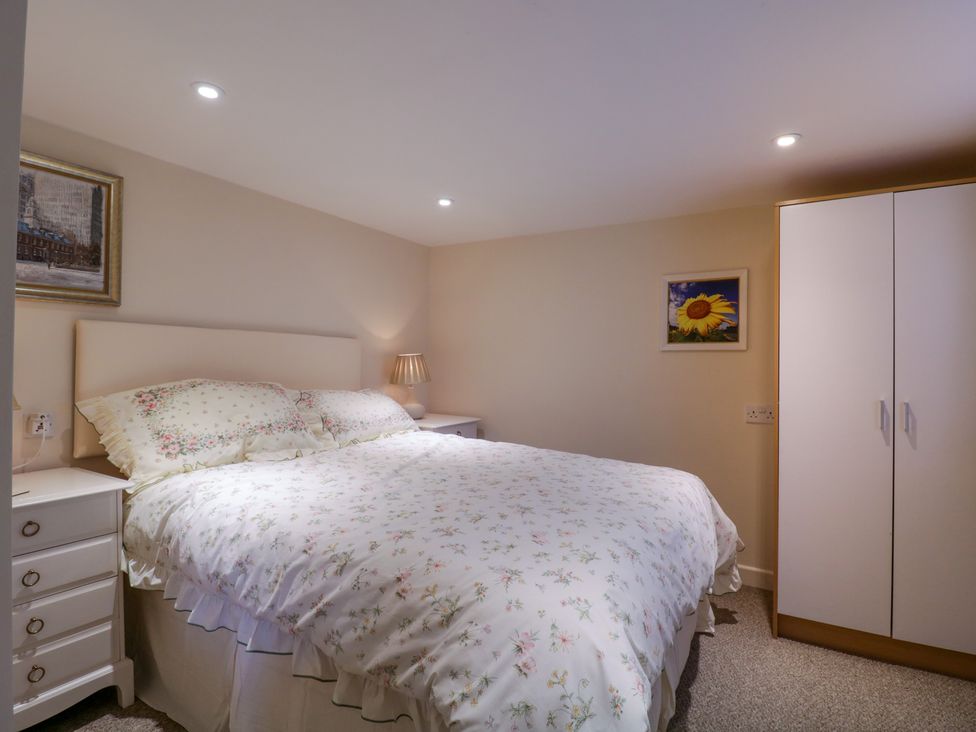 A bedroom with a bed with floral bedding two bedside tables with lamps a wardrobe and framed pictures on the walls at The Cottage in Sudbury