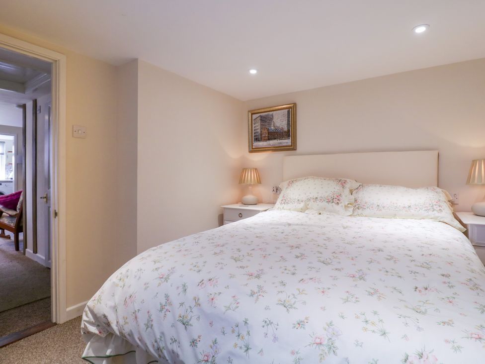 A bedroom with a double bed and floral bedding two bedside tables with lamps and a framed picture on the wall at The Cottage in Sudbury
