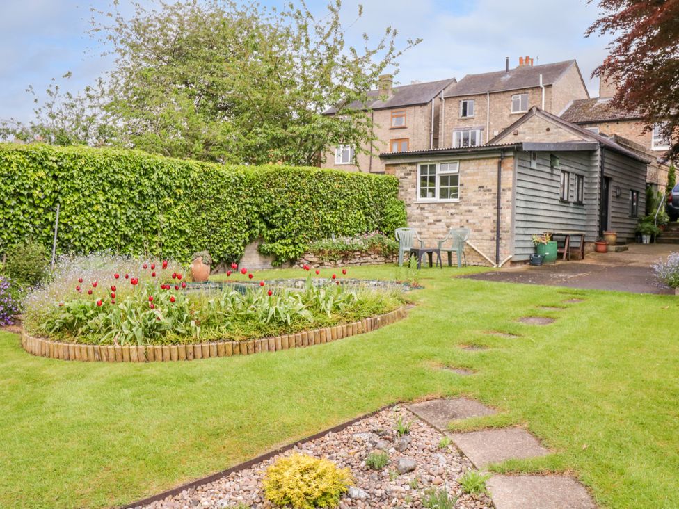 A garden with flower beds lawn and a shed with plastic chairs outside at The Cottage in Sudbury