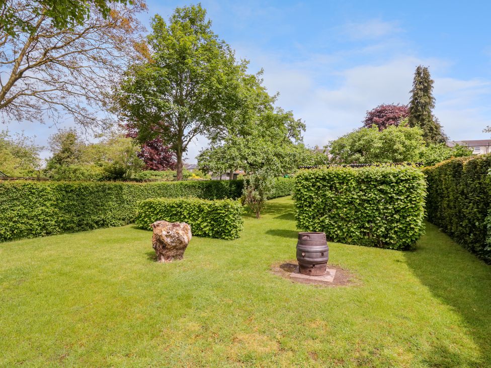 A garden with trimmed hedges trees green grass and a barrel at The Cottage in Sudbury