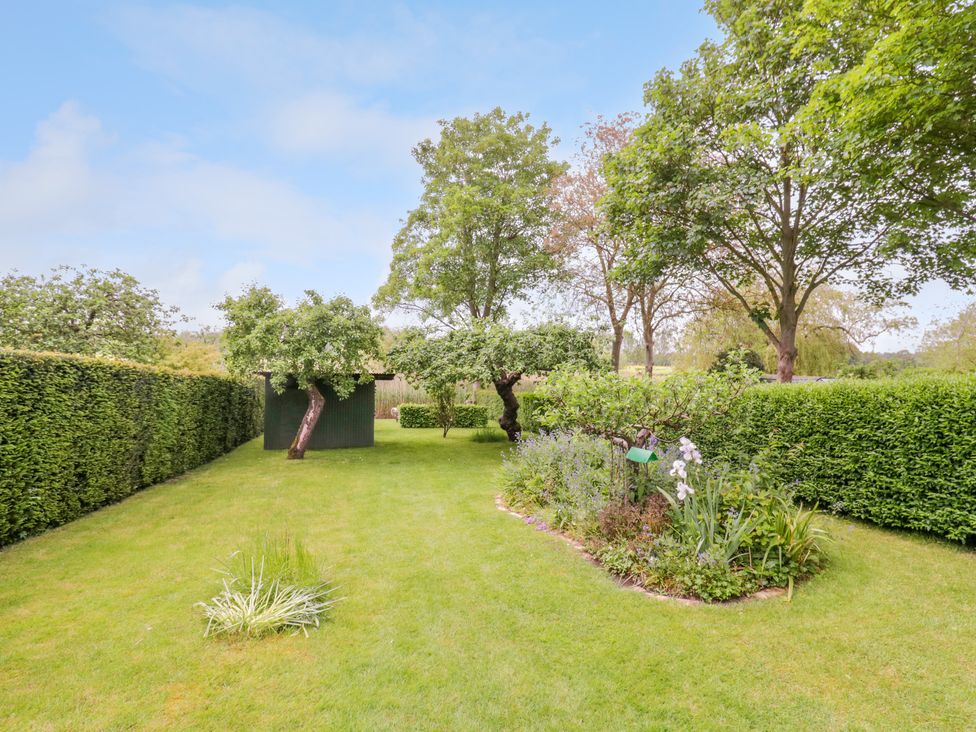 A garden with a lawn hedge trees and a flower bed at The Cottage in Sudbury