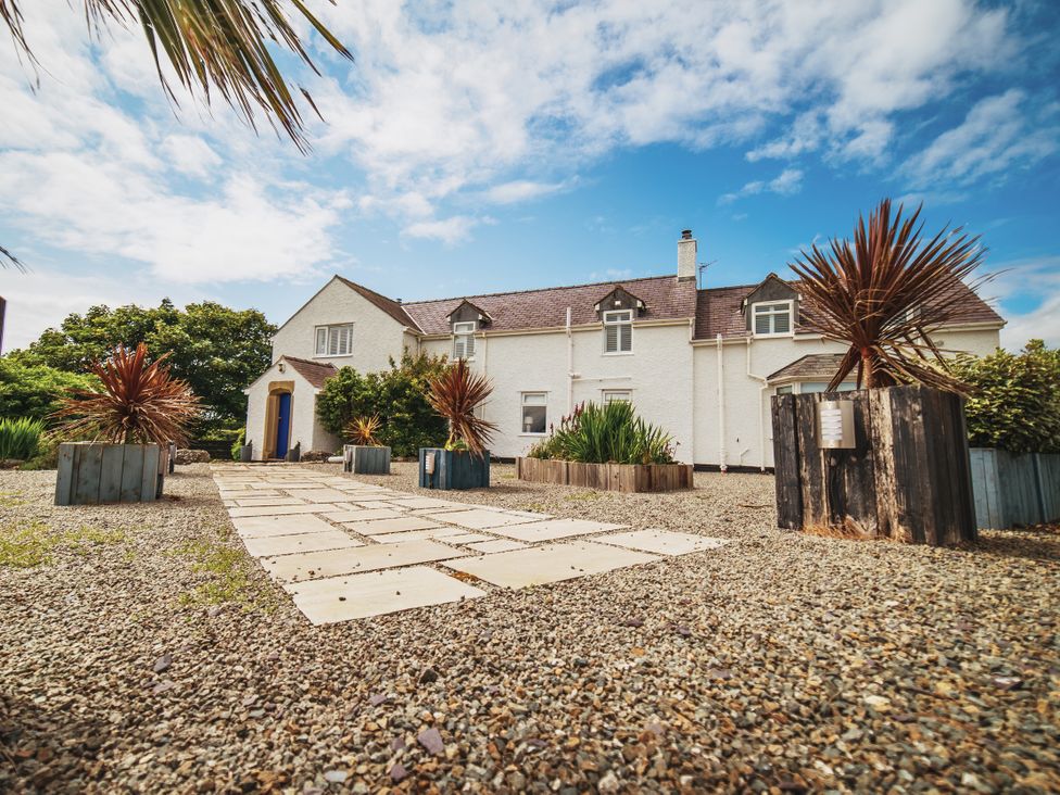 An outdoor view of a house with a gravel pathway and planters at Glanllyn Bach in Llanfaelog