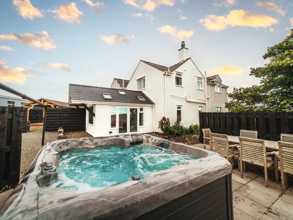 An outdoor area with a hot tub and seating near the house at Glanllyn Bach Llanfaelog