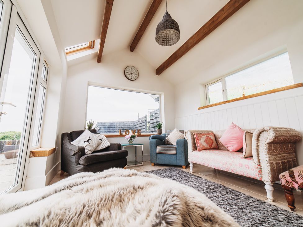 A living room with a sofa, armchair, and coffee table at Glanllyn Bach in Llanfaelog