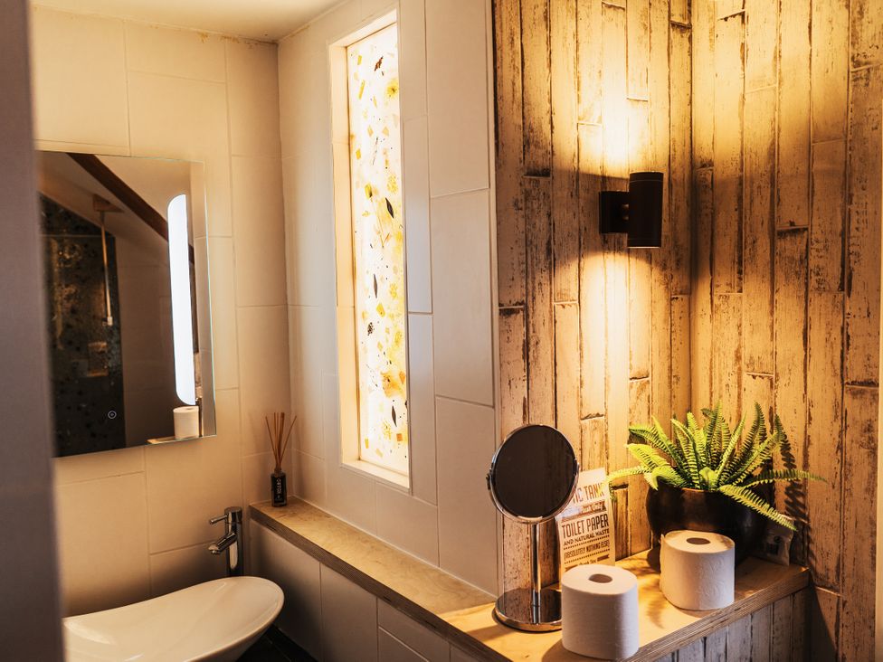 A bathroom featuring a toilet, mirror, and sink at Glanllyn Bach in Llanfaelog