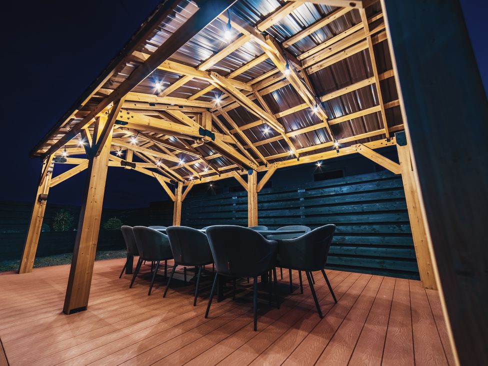 An outdoor dining area with a wooden pergola and chairs at Glanllyn Bach in Llanfaelog