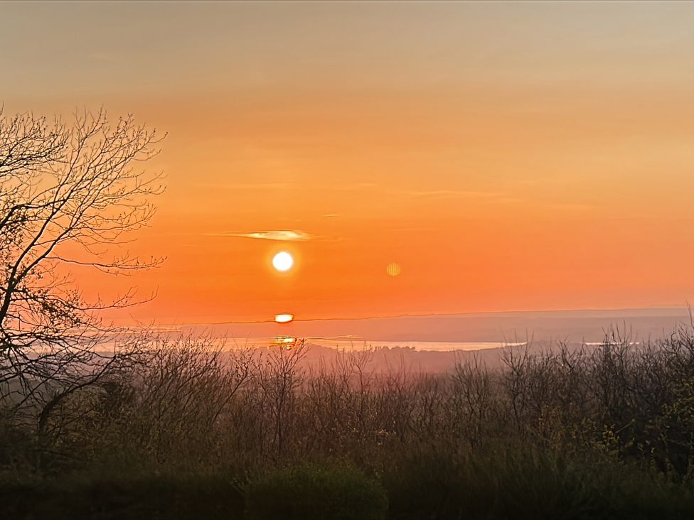 A sunset view with trees and water at Tan Y Merddyn in Ceunant near Llanrug